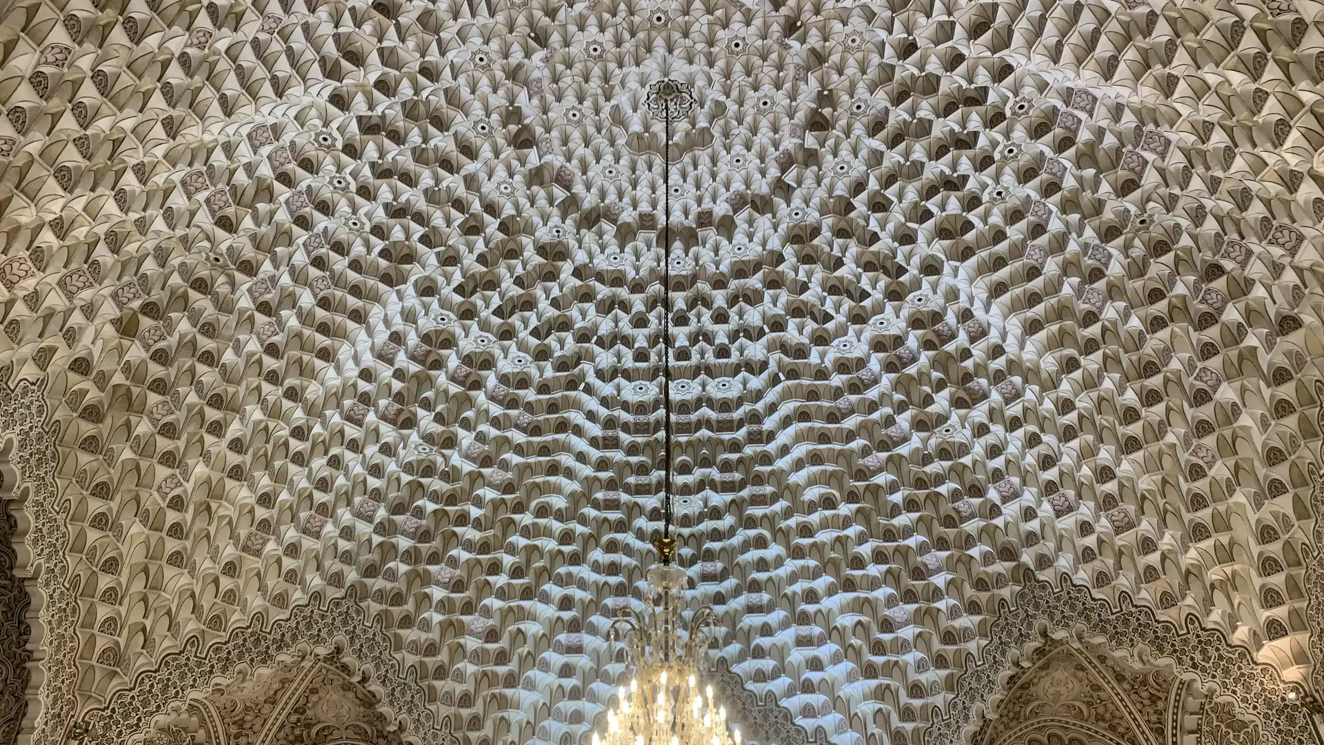 نمای رو به بالا از سقف مقرنس سفید و پرنقش یک مسجد با نور ملایم و یک چلچراغ؛ تصویری برای مقاله‌ی چشم سوم در قرآن و عرفان اسلامی